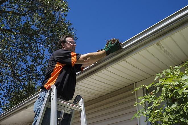 workman on a ladder repairing a broken gutter in Dayton